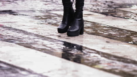 Super-slow-motion-footage-of-black-high-heel-boots-walking-across-a-wet-crosswalk-in-the-rain