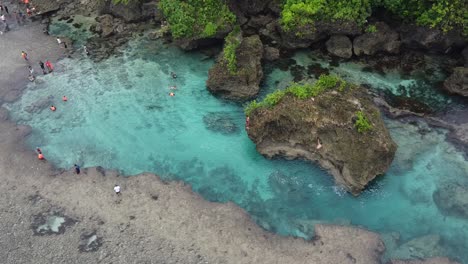 People-swim-in-clear-blue-water-of-Magpopongko-tidal-rock-pool,-Siargao
