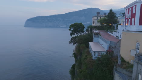 Aerial-footage-of-houses-and-trees-on-the-cliff-in-the-city-of-Sorrento,-Italy,-revealing-a-bay-of-water-beyond