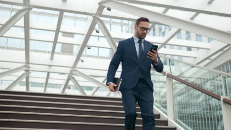 Worrying-Caucasian-Male-Office-Worker-Rushing-Down-the-Steps-on-His-Business-With-Notebook-Looking-at-Phone-Screen