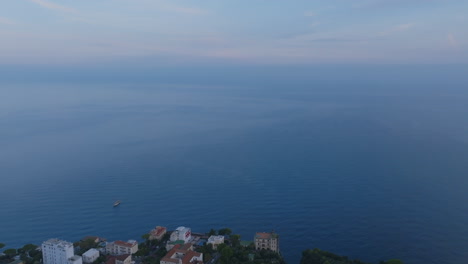 Aerial-footage-in-the-early-morning-of-a-boat-off-the-coast-of-Sorrento,-Italy-and-then-revealing-more-of-the-town-on-the-cliffs-by-the-sea