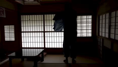 Silhouette-Eines-Mannes,-Der-Aufwacht-Und-Ein-Kimono-Hemd-In-Einem-Schwach-Beleuchteten-Ryokan-Mit-Hintergrundbeleuchteten-Shoji-Türen-Anzieht