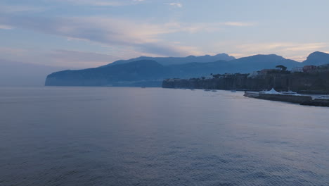 Flying-over-the-water-of-the-Mediterranean-Sea-towards-the-town-of-Sorrento,-Italy-in-the-morning-light