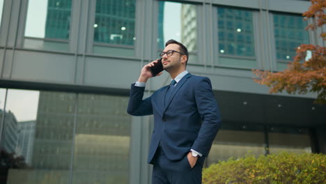 Businessman-Talking-on-Phone-Standing-Outside-Modern-Office-Building---low-angle-parallax-shot