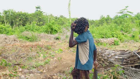 Junger-Schwarzer-Bauer,-Der-Auf-Seiner-Schulter-Eine-Junge-Kokosnuss-In-Zeitlupe-Trägt-Und-Eine-Feldfarm-In-Afrika-überquert