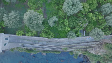 Top-down-aerial-footage-of-trees-that-moves-over-the-cliff-face-and-shows-stairs-that-go-down-to-the-Mediterranean-Sea-in-the-town-of-Sorrento,-Italy
