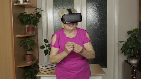 Senior-grandmother-woman-in-virtual-headset-glasses-watching-3d-video-in-360-vr-helmet-at-home