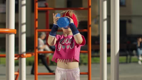 Girl-in-sportswear-drinking-water-for-refreshment-after-fitness-exercises.-Little-athletic-child