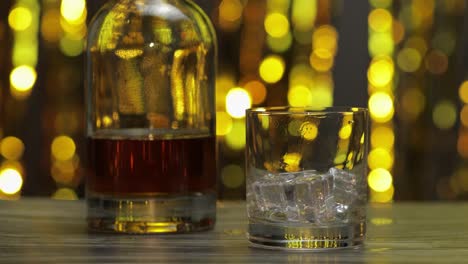 Vertido-De-Whisky-Dorado,-Coñac-O-Brandy-De-La-Botella-Al-Vaso-Con-Cubitos-De-Hielo.-Fondo-Brillante
