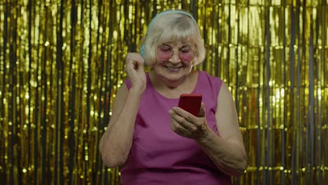 Elegante-Y-Feliz-Anciana-Sosteniendo-Un-Teléfono-Celular,-Escuchando-Música-Con-Auriculares-Y-Bailando