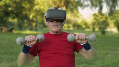 Senior-old-grandfather-man-in-VR-headset-helmet-making-fitness-exercises-with-dumbbells-in-park