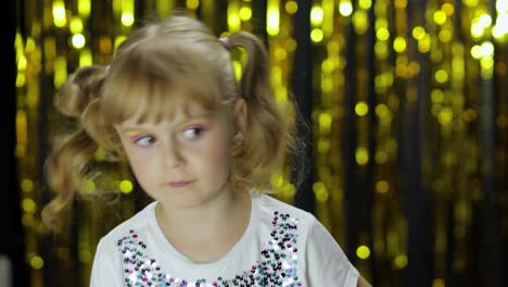 Stylish-child-dancing-fooling-around,-make-faces.-Girl-posing-on-background-with-foil-golden-curtain
