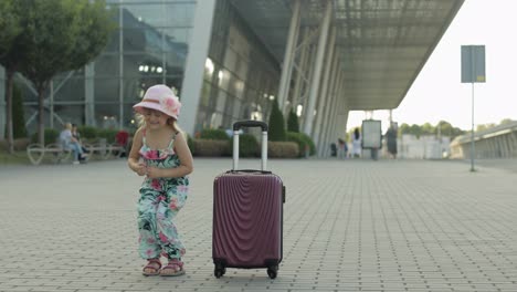 Child-girl-tourist-with-suitcase-bag-near-airport.-Small-kid-dance,-jump,-celebrate-with-luggage