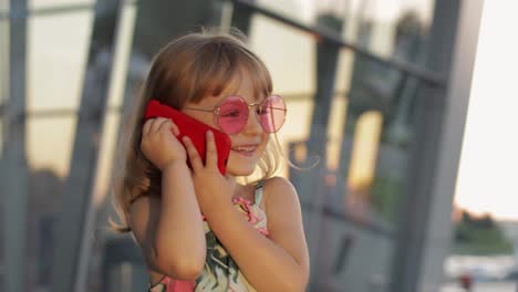 Tourist-kid-girl-wearing-trendy-sunglasses-use-phone.-Child-using-smartphone-for-call,-talk.-Tourism