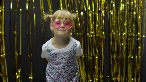 Child-dancing,-pointing-fingers-at-camera.-Girl-posing-on-background-with-foil-golden-curtain