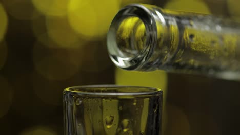 Barman-pour-frozen-vodka-from-bottle-into-shot-glass-against-shiny-gold-party-celebration-background