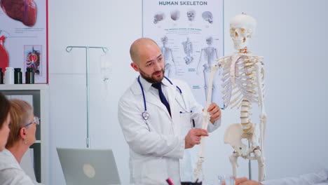 Médico-Especialista-Que-Muestra-Las-Funciones-óseas-Del-Cuerpo-Usando-Un-Modelo-De-Esqueleto