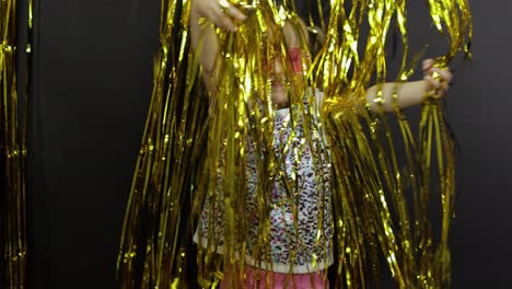 Happy-child-dancing,-playing,-fooling-around-in-shiny-foil-fringe-golden-curtain.-Little-blonde-kid
