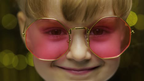 Close-up-face-of-child.-Smiling,-looking-at-camera.-Girl-in-pink-sunglasses-posing