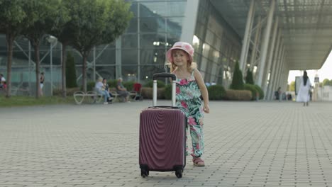 Child-girl-tourist-with-suitcase-bag-near-airport.-Kid-dances,-rejoices,-celebrates-with-luggage