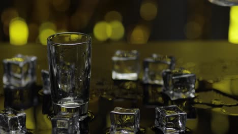 Barman-pour-frozen-vodka-from-bottle-into-shot-glass.-Ice-cubes-against-shiny-gold-party-background