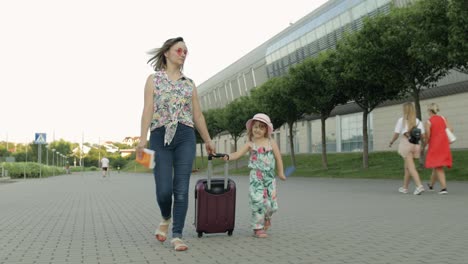 Mother-and-daughter-walking-outdoors-to-airport.-Woman-carrying-suitcase-bag.-Child-and-mom-vacation