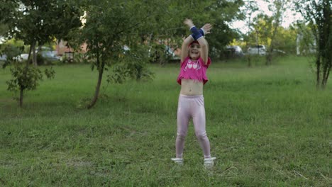 Young-cute-child-girl-in-sportswear-making-fitness-jump-exercises-outdoors-in-park.-Workout-for-kids