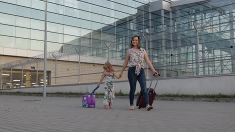 Mother-and-daughter-walking-from-airport.-Woman-and-child-carrying-suitcase-bags.-Mom-after-vacation