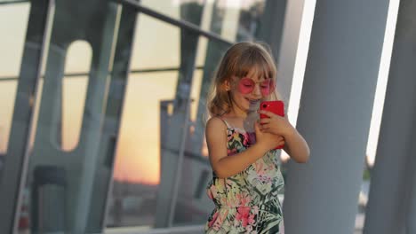 Tourist-kid-girl-wearing-trendy-sunglasses-use-phone.-Child-using-smartphone-for-video-call,-selfie