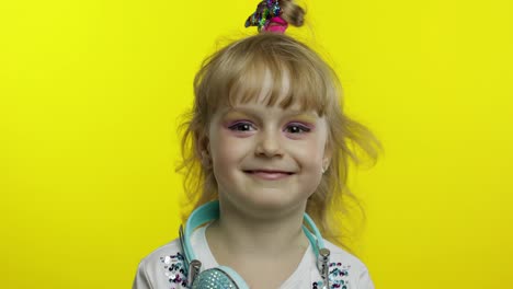 Child-smiling,-looking-at-camera.-Girl-with-headphones-on-the-neck-posing-on-yellow-background