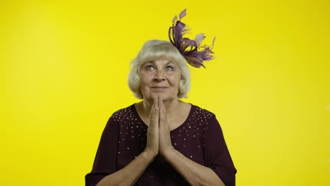 Positive-senior-old-blond-woman-appealing-to-camera,-keeping-prayer-gesture-and-asking-help