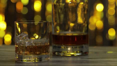 Barmann-Schiebt,-Stellt-Glas-Mit-Goldenem-Whiskey,-Cognac-Oder-Brandy-Mit-Eiswürfeln-Auf-Den-Holztisch
