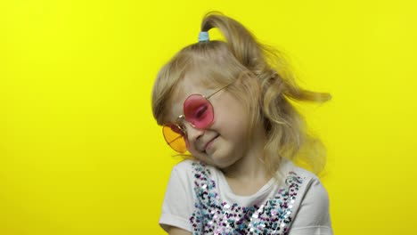 Child-smiling,-looking-at-camera.-Girl-tourist-in-pink-sunglasses-posing-on-yellow-background