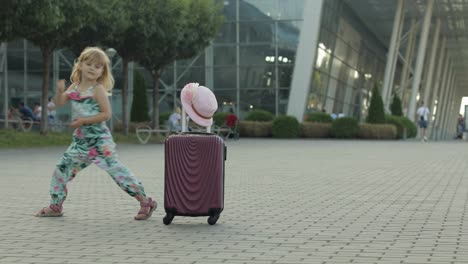Child-girl-tourist-with-suitcase-bag-near-airport.-Kid-dances,-rejoices,-celebrates-with-luggage