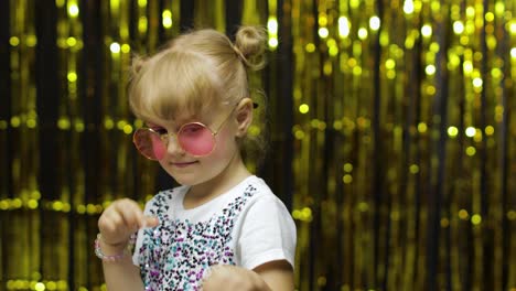Child-smiling,-pointing-fingers-at-camera.-Girl-posing-on-background-with-foil-golden-curtain