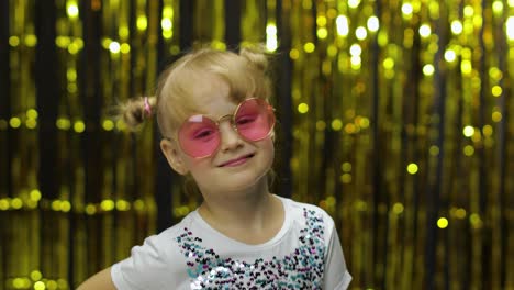 Child-smiling,-looking-at-camera.-Girl-in-pink-sunglasses-posing-on-background-with-foil-curtain