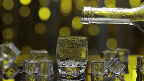 El-Barman-Vierte-Vodka-Congelado-De-La-Botella-En-Un-Vaso-De-Chupito.-Cubitos-De-Hielo-Sobre-Fondo-De-Fiesta-Dorado-Brillante