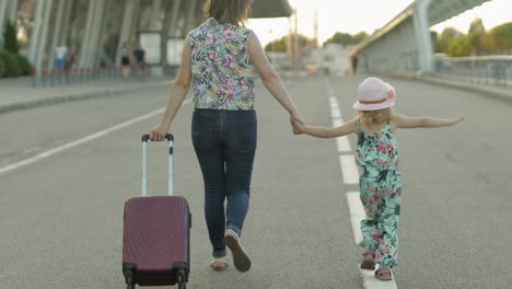 Mother-and-daughter-walking-outdoors-to-airport.-Woman-carrying-suitcase-bag.-Child-and-mom-vacation