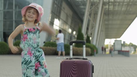 Child-girl-tourist-with-suitcase-luggage-bag-near-airport.-Kid-dances,-rejoices,-celebrates