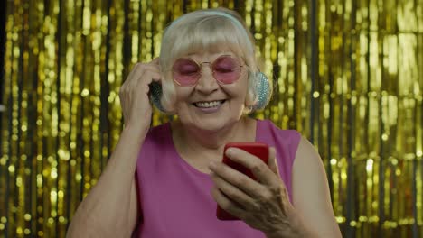 Stilvolle,-Glückliche-ältere-Frau-Hält-Ihr-Handy-In-Der-Hand,-Hört-Musik-über-Kopfhörer-Und-Tanzt