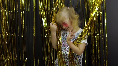 Happy-child-dancing,-playing,-fooling-around-in-shiny-foil-fringe-golden-curtain.-Little-blonde-girl