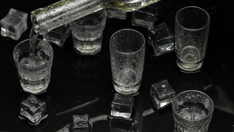 Barmann-Gießt-Gefrorenen-Wodka-Aus-Der-Flasche-In-Ein-Schnapsglas.-Eiswürfel-Vor-Dunklem,-Nassem-Schwarzem-Hintergrund