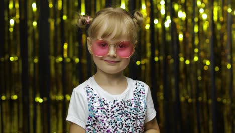 Child-show-ok-sign,-smiling,-looking-at-camera.-Girl-posing-on-background-with-foil-golden-curtain