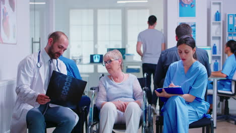 Arzt-Hält-Röntgenbild-Einer-Behinderten-Seniorin-Im-Rollstuhl