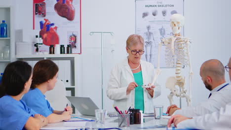 Ältere-Ärztin-Zeigt-Die-Arbeit-Der-Menschlichen-Hand-Am-Skelettmodell