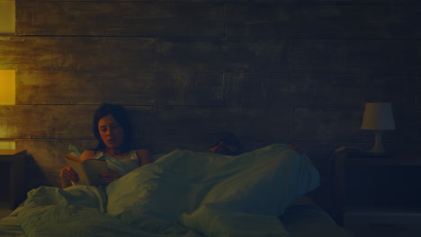 Woman-reading-a-book-in-bed-at-night-lamp