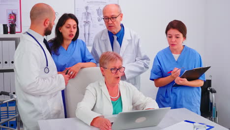 Medical-practitoner-working-on-laptop-during-briefing-with-coworkers