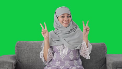 Fröhliche-Muslimische-Frau-Zeigt-Siegeszeichen-Auf-Grünem-Bildschirm