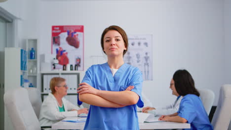 Enfermera-Mirando-La-Cámara-Sonriendo-De-Pie-En-La-Oficina-De-La-Conferencia-Médica