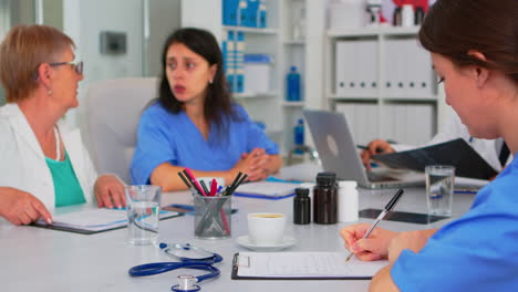 Krankenschwester-Schreibt-In-Die-Zwischenablage,-Während-Professionelle-Teamarbeiter-Ein-Medizinisches-Treffen-Abhalten